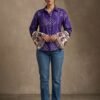 Full-length view of a woman wearing a purple printed bell sleeve shirt with blue jeans and heels.