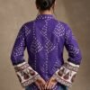 Back view of a woman wearing a purple printed bell sleeve shirt with ethnic sleeve border detailing and blue jeans.