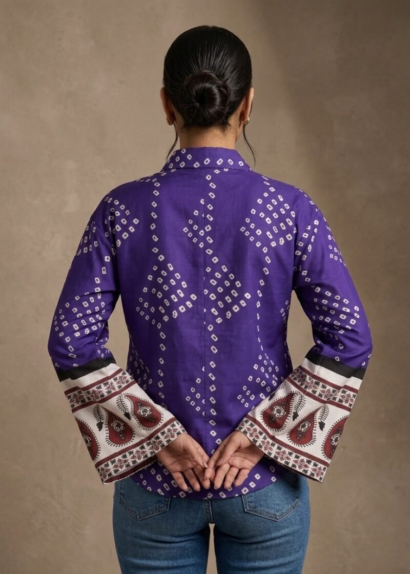 Back view of a woman wearing a purple printed bell sleeve shirt with ethnic sleeve border detailing and blue jeans.