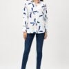 Full-length front view of a women's white printed shirt featuring abstract navy blue and blush pink floral motifs, styled with dark blue skinny jeans and nude high heels.